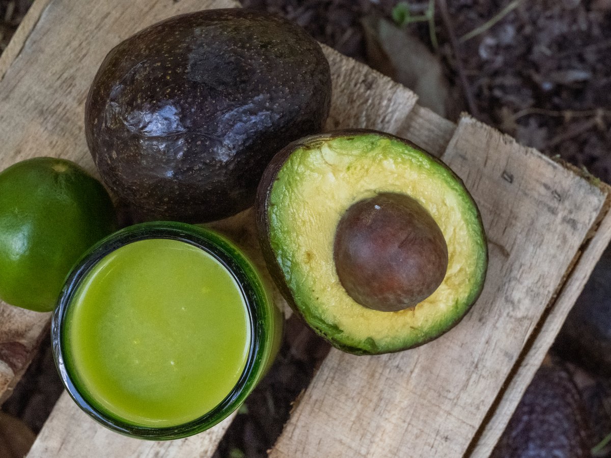 Aguacate partido y un vaso de agua de aguacate sobre madera